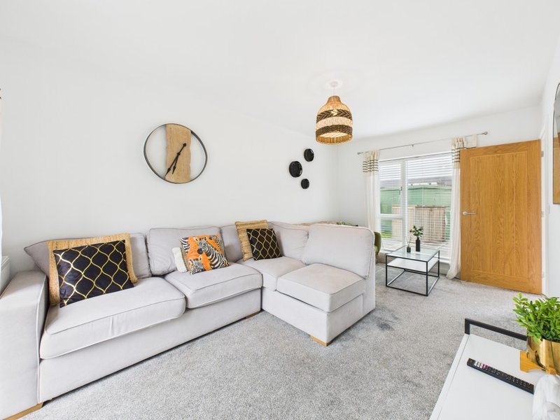 Bright living room with light gray sectional sofa, patterned cushions, pendant lighting, and wooden door