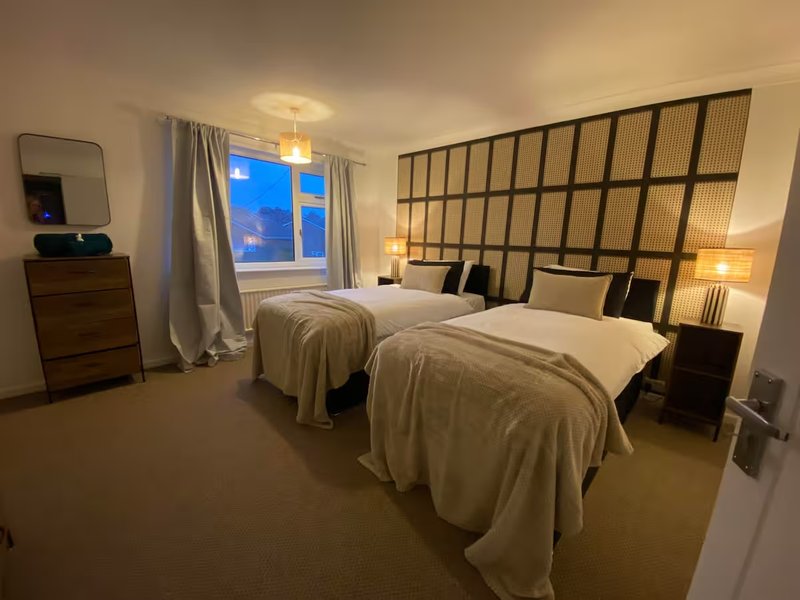 Modern bedroom with two single beds, geometric headboard, bedside lamps and window view