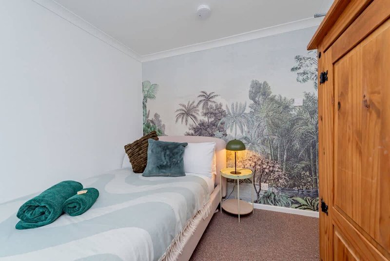 Bedroom with single bed, tropical wallpaper, teal cushions and bedside lamp