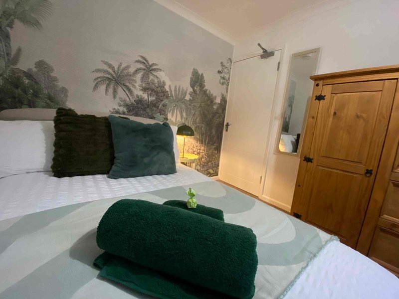Bedroom with double bed, green cushions and rolled towels, tropical wall mural, wooden door