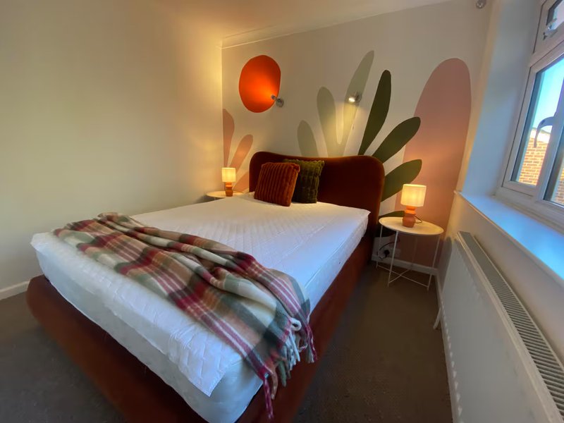 Bedroom with double bed, burgundy headboard, wall-mounted cactus decor, and warm lighting