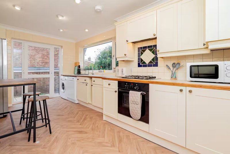 Bright modern kitchen with cream cabinets, wooden worktops, black range cooker, and dining area with bar stools