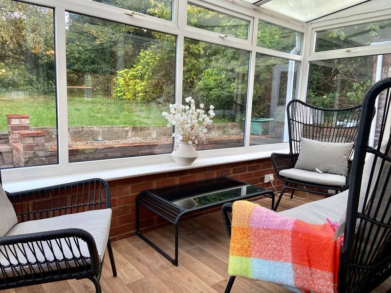 Sunroom with wicker chairs, coffee table, colorful throw blanket and garden views