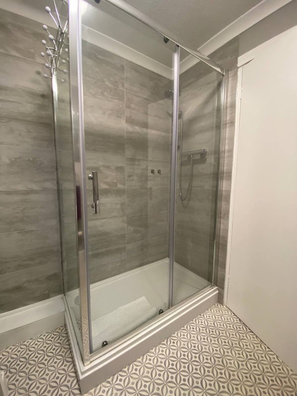 Modern bathroom with glass-enclosed shower, gray tile walls, and geometric floor pattern