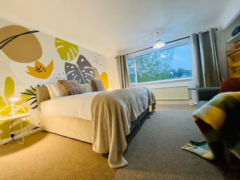Bright bedroom with single bed, geometric wall art, window with garden view, and seating area