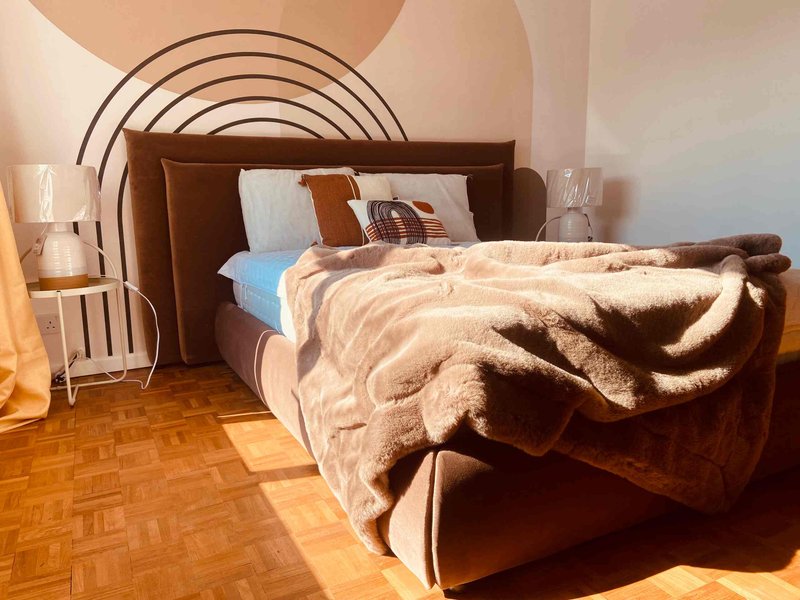 Bedroom with metal bed frame, rumpled bedding, pillows, wooden floor and wall art