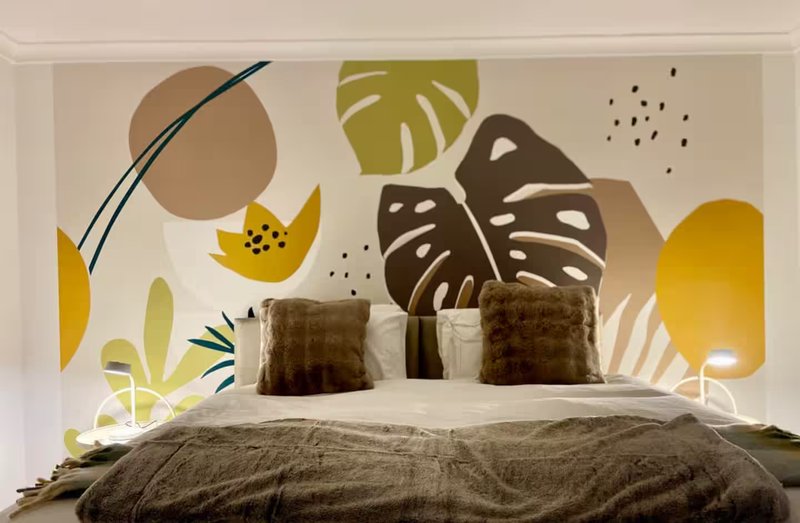 Bedroom with double bed, brown and cream bedding, decorative wall mural with botanical leaf shapes
