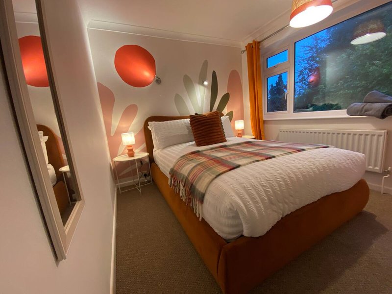 Modern bedroom with orange-upholstered bed, decorative wall lights, and large windows overlooking garden