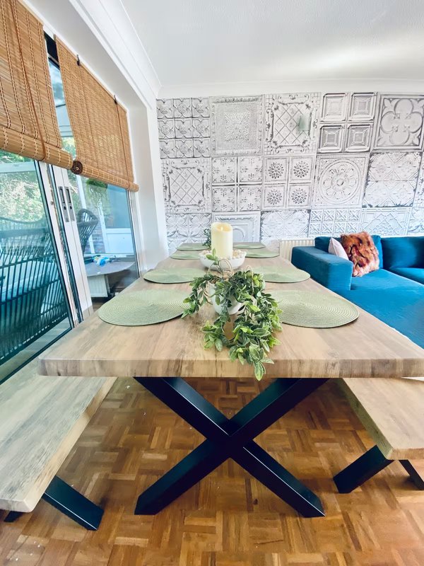 Modern dining room with wooden table, blue base, place settings, green centerpiece and blue sofa