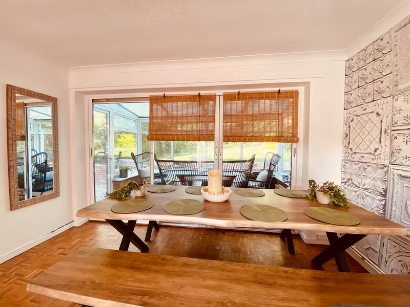 Dining room with wooden table, parquet flooring, large windows and woven blinds