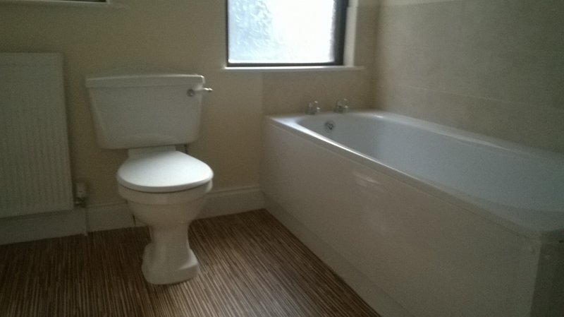 Bathroom with white toilet, bathtub, striped brown flooring and window