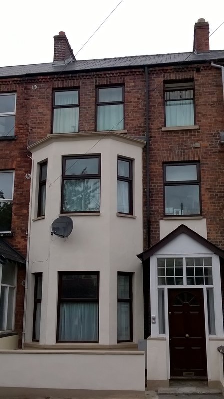 Brick terraced house with cream bay window, red door, and chimney stacks