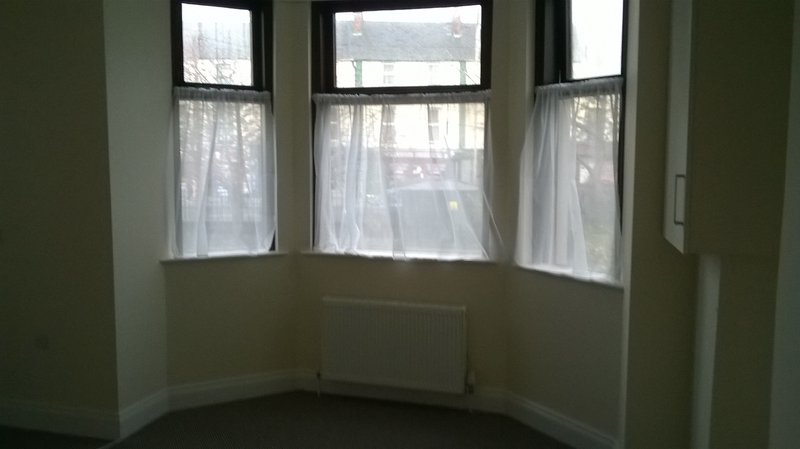 Bay window with sheer curtains, radiator and white walls in empty room