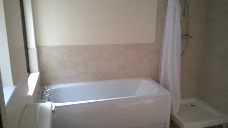 Bathroom with white bathtub, beige tile walls, and window with curtains