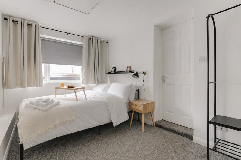 Bright bedroom with single bed, wooden nightstand, window with curtains and blinds