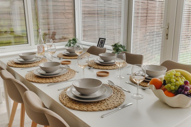 Dining table set for four with place settings, glasses, and fresh fruit bowl by window