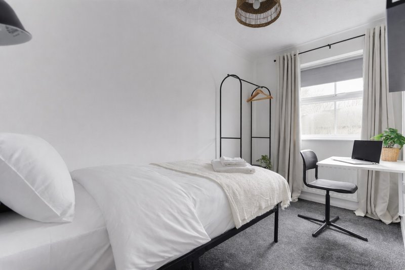 Bright bedroom with single metal-frame bed, white bedding, desk, chair and window