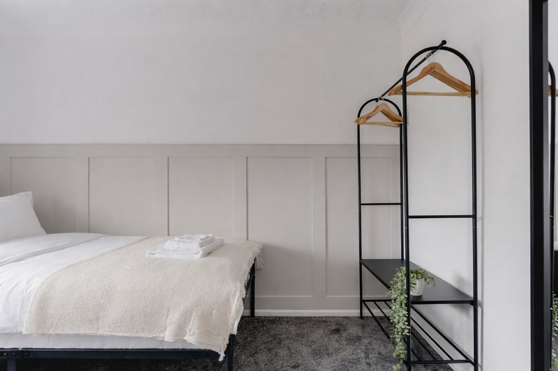 Minimalist bedroom with white bedding, panelled headboard, metal coat rack and wooden hangers
