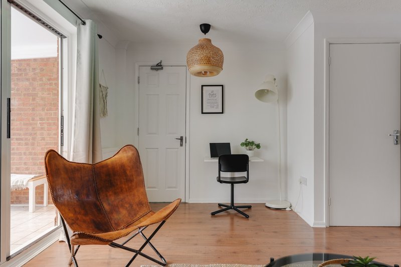 Modern studio with brown leather butterfly chair, wooden floor, desk chair and rattan pendant light