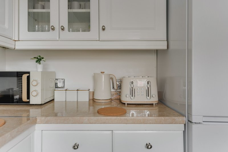 Modern kitchen countertop with white appliances, wooden worktop and white cabinetry