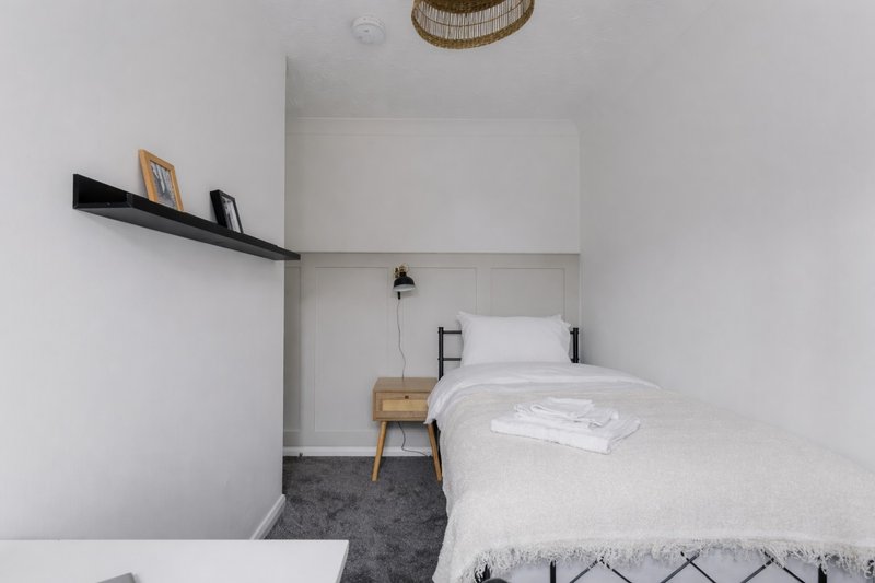 Minimalist bedroom with single bed, wooden nightstand, black floating shelf and woven pendant light