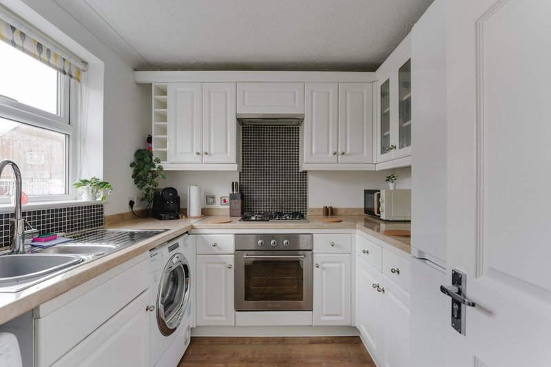 Modern white kitchen with built-in appliances, wooden worktops, and window overlooking garden