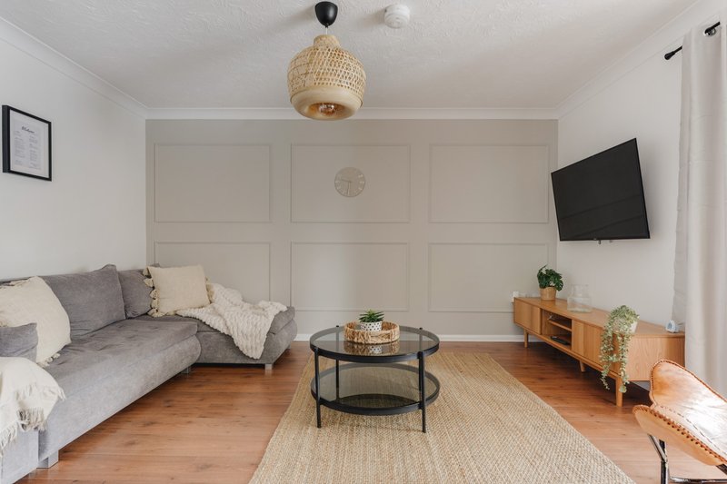 Bright living room with grey sofa, round black coffee table, wooden TV stand and woven pendant lamp