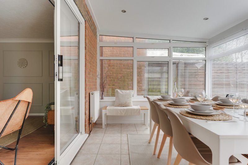 Bright dining area with set table, chairs, and garden-facing windows with brick exterior