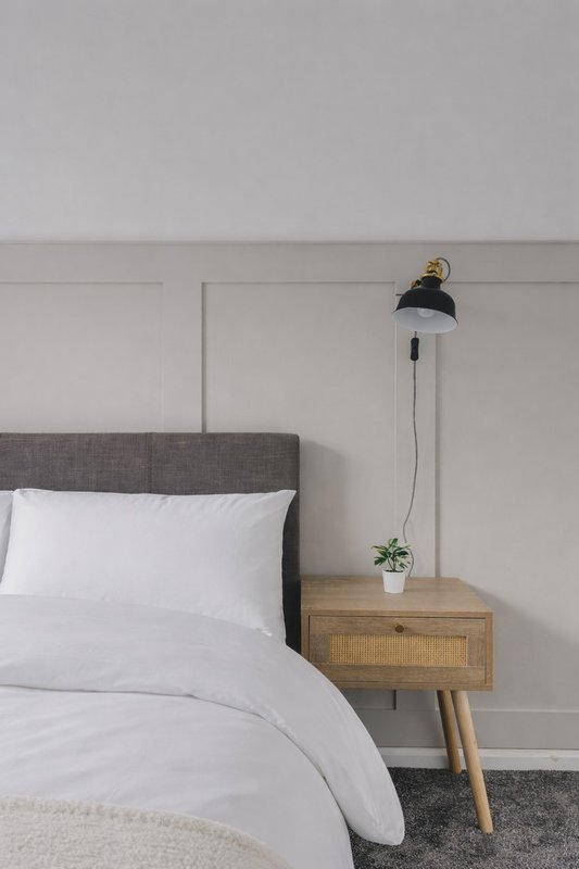 Bedroom with gray upholstered headboard, white bedding, wooden nightstand and black pendant lamp