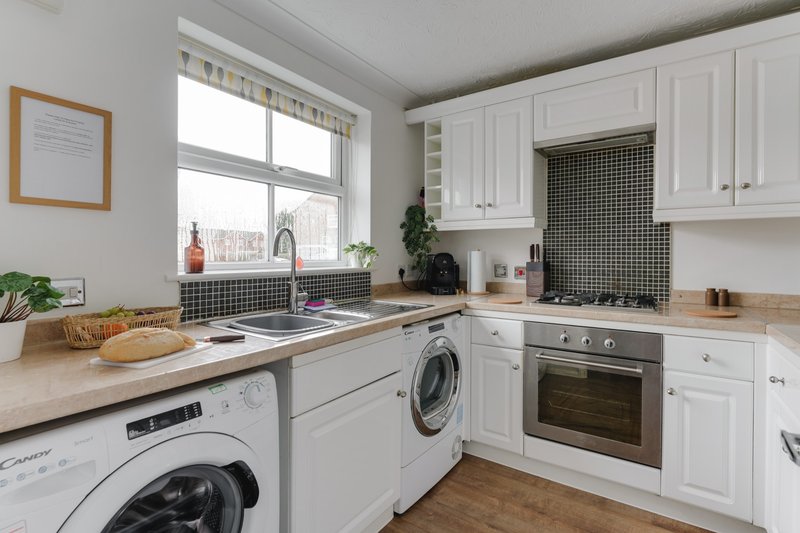 Modern kitchen with white cabinetry, integrated appliances, wooden worktops and bright window