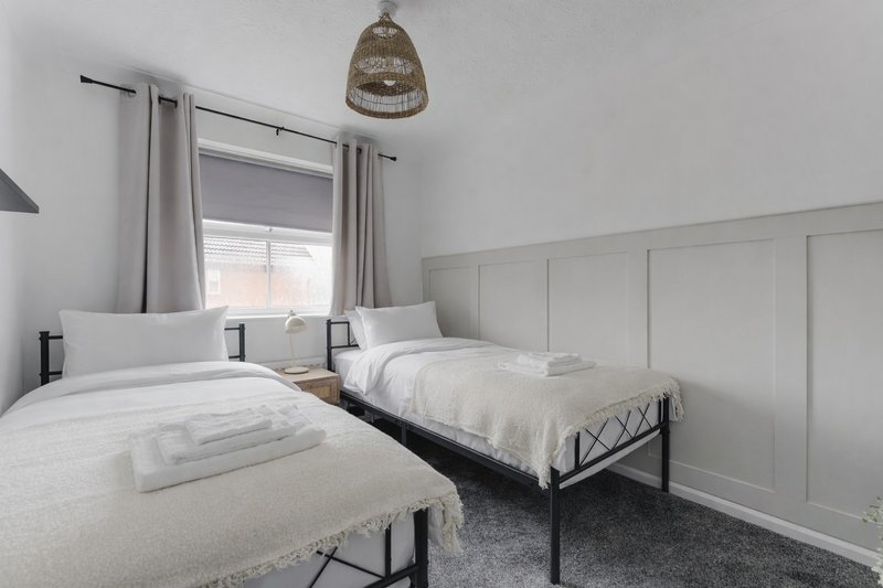 Bright bedroom with two single beds, white bedding, woven pendant light and window