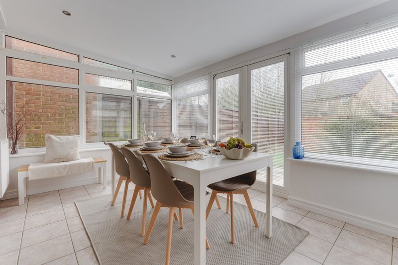 Modern dining area with white table, wooden chairs, bench seating and large windows overlooking garden