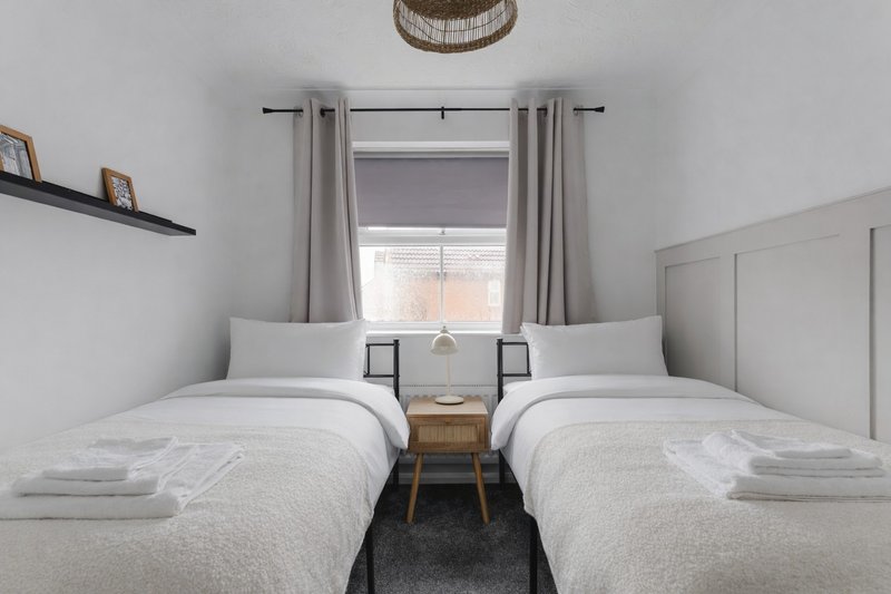 Twin bedroom with two single beds, bedside table, window with curtains and woven pendant light