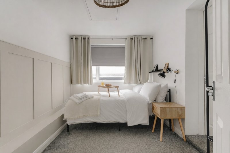 Bright minimalist bedroom with white bedding, wooden nightstand, and window with neutral curtains