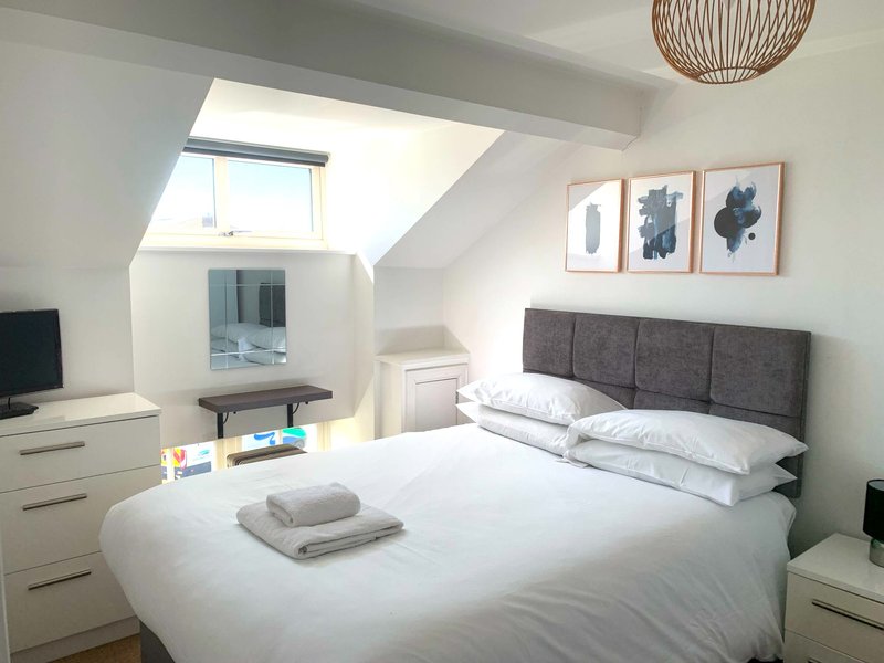 Bright attic bedroom with double bed, grey headboard, white bedding, skylight and wooden pendant lamp