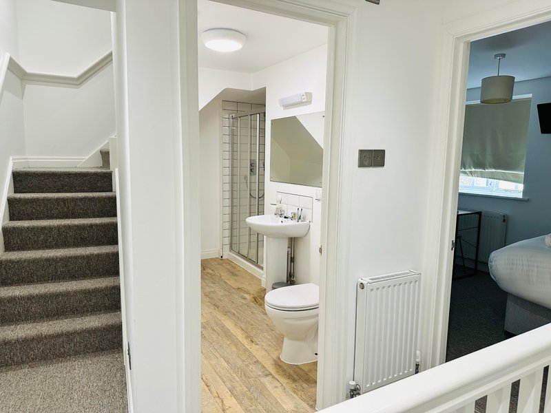 Landing area with stairs, bathroom doorway, toilet visible, wooden flooring and white walls