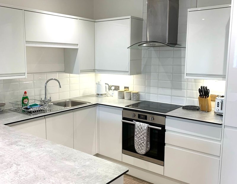 Modern white kitchen with marble countertops, built-in oven, and stainless steel extractor hood