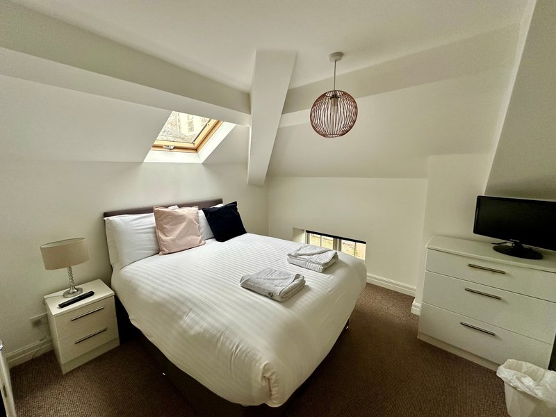 Bright attic bedroom with double bed, skylight window, pendant light, and white furniture