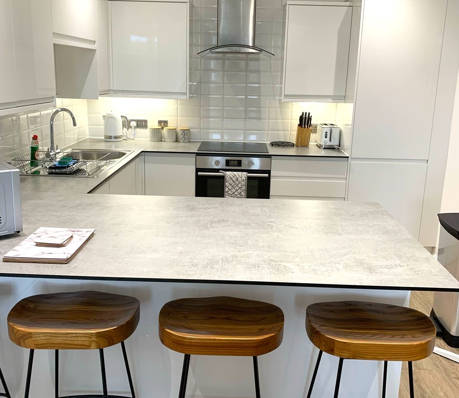 Modern white kitchen with island, wooden bar stools, built-in appliances and tile backsplash