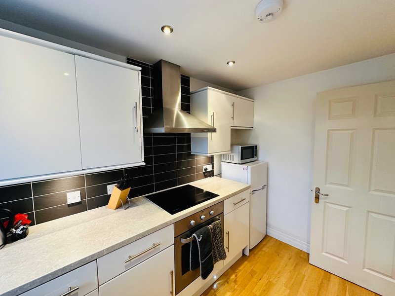 Modern kitchen with cream cabinets, black tile backsplash, induction cooktop and wooden flooring