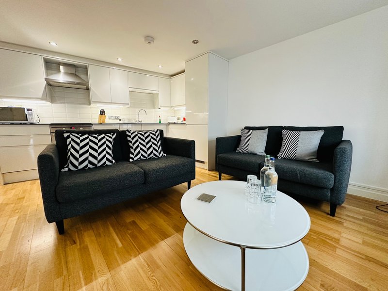 Open-plan living area with black sofas, white coffee table, and modern kitchen with white cabinetry