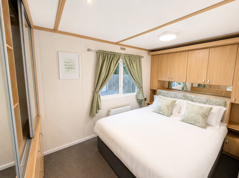 Bright bedroom with double bed, wooden furniture, green curtains and wall art