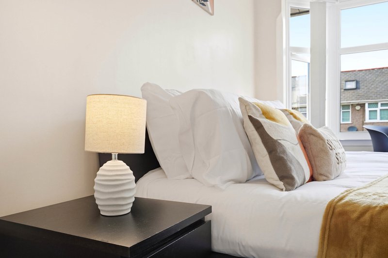 Bright bedroom with white bed, decorative pillows, bedside lamp and windows overlooking street