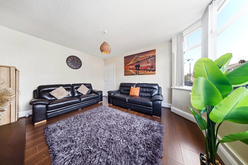 Bright living room with two black leather sofas, grey rug, wooden floor and large windows