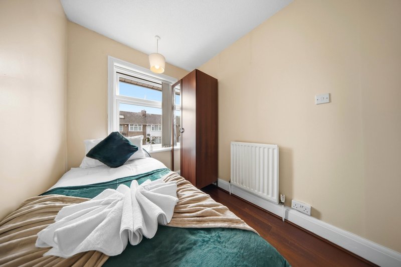 Compact bedroom with single bed, dark wooden wardrobe, and window overlooking street