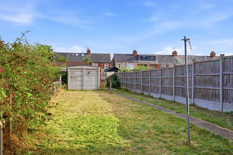 Residential garden with lawn, wooden fencing, shed and neighbouring houses in background