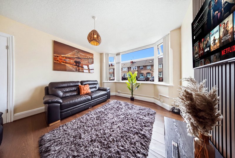 Bright living room with dark leather sofa, gray rug, pendant lamp, and large window overlooking street