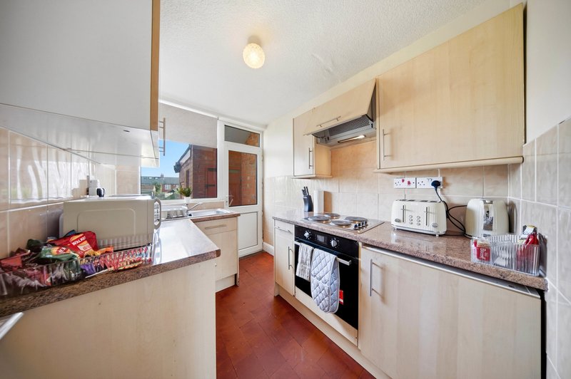 Compact kitchen with light wood cabinets, gas hob, and red tile flooring