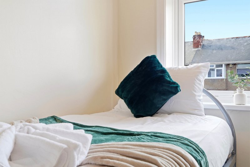 Bedroom with single bed, white pillows, dark teal cushion and green throw blanket, window with countryside view