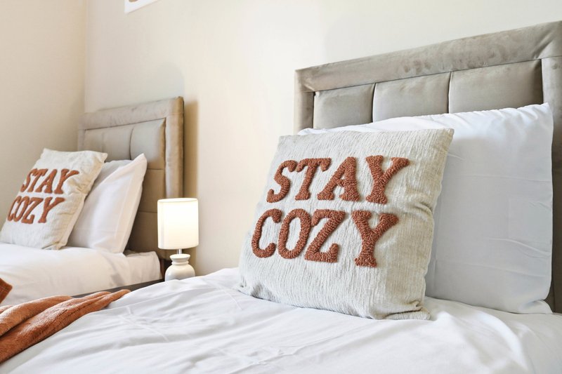 Bedroom with two beds, gray upholstered headboards, white bedding, and decorative cushions